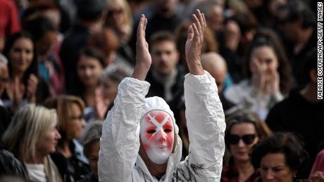 A protester wearing a mask with the image of syringes and a full protective suit applauds in Geneva on October 9, 2021.