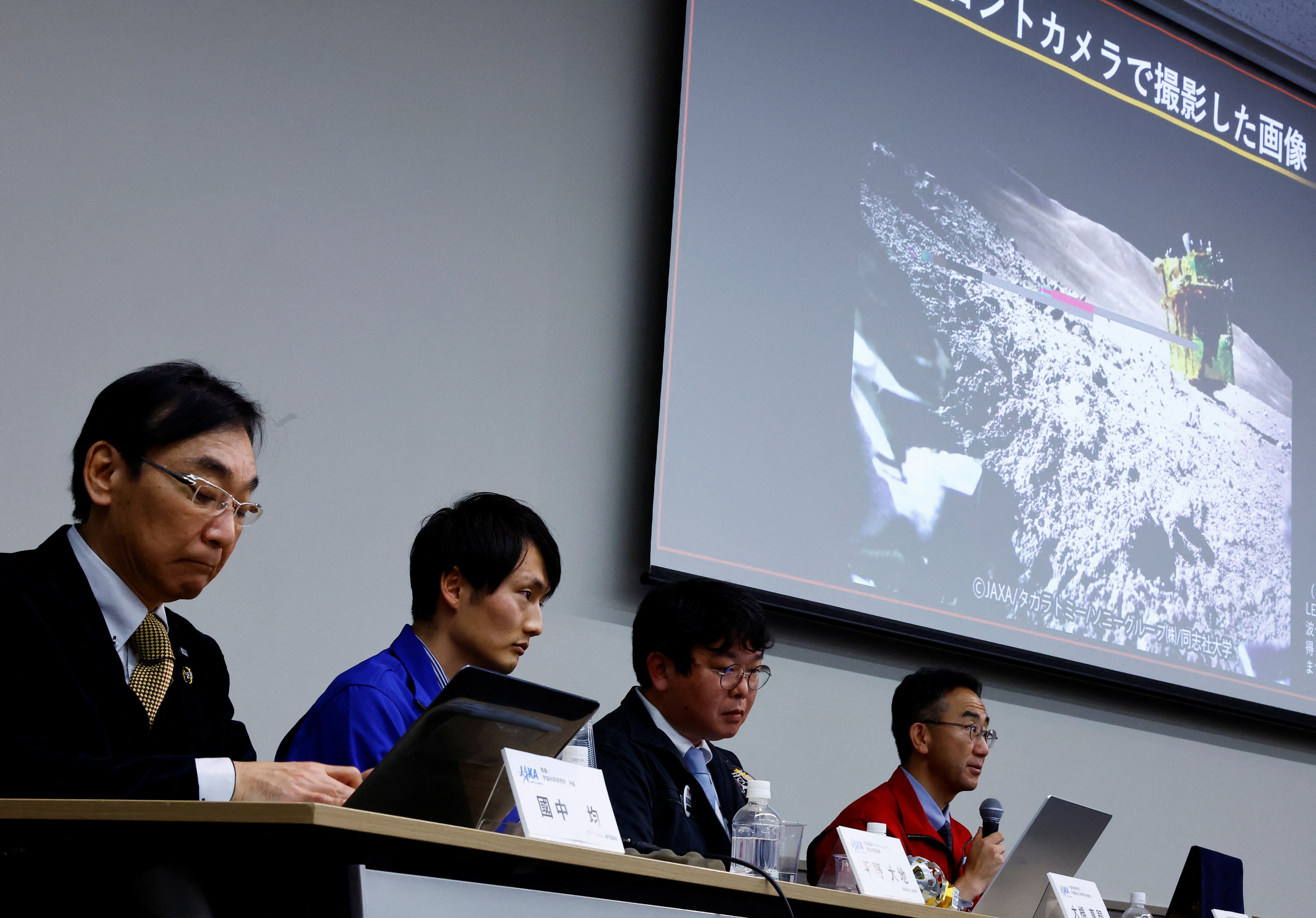 Hitoshi Kuninaka, Daichi Hirano, Masatsugu Otsuki and Shinichiro Sakai of JAXA sit in front of a screen showing an image taken by LEV-2 on the moon, during a press conference on SLIM's moon landing mission in Tokyo, Japan, January 25, 2024 (Image: Reuters)